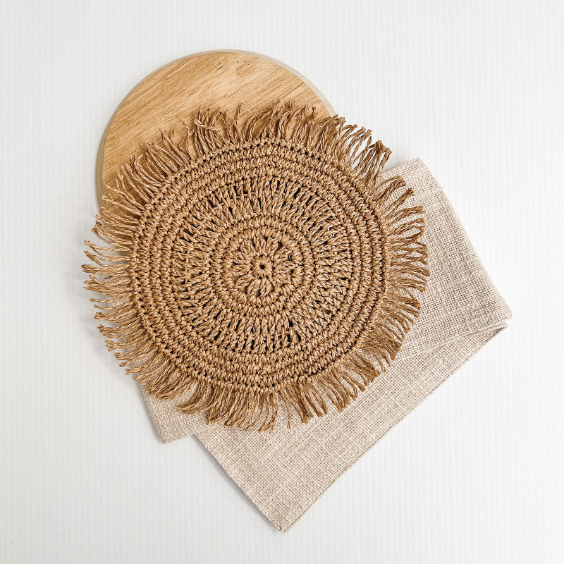 White boho cushion with stone natural colour strip wrapped around the cushion with a woven raffia disk attached to the front. The perfect Boho Accessory.
